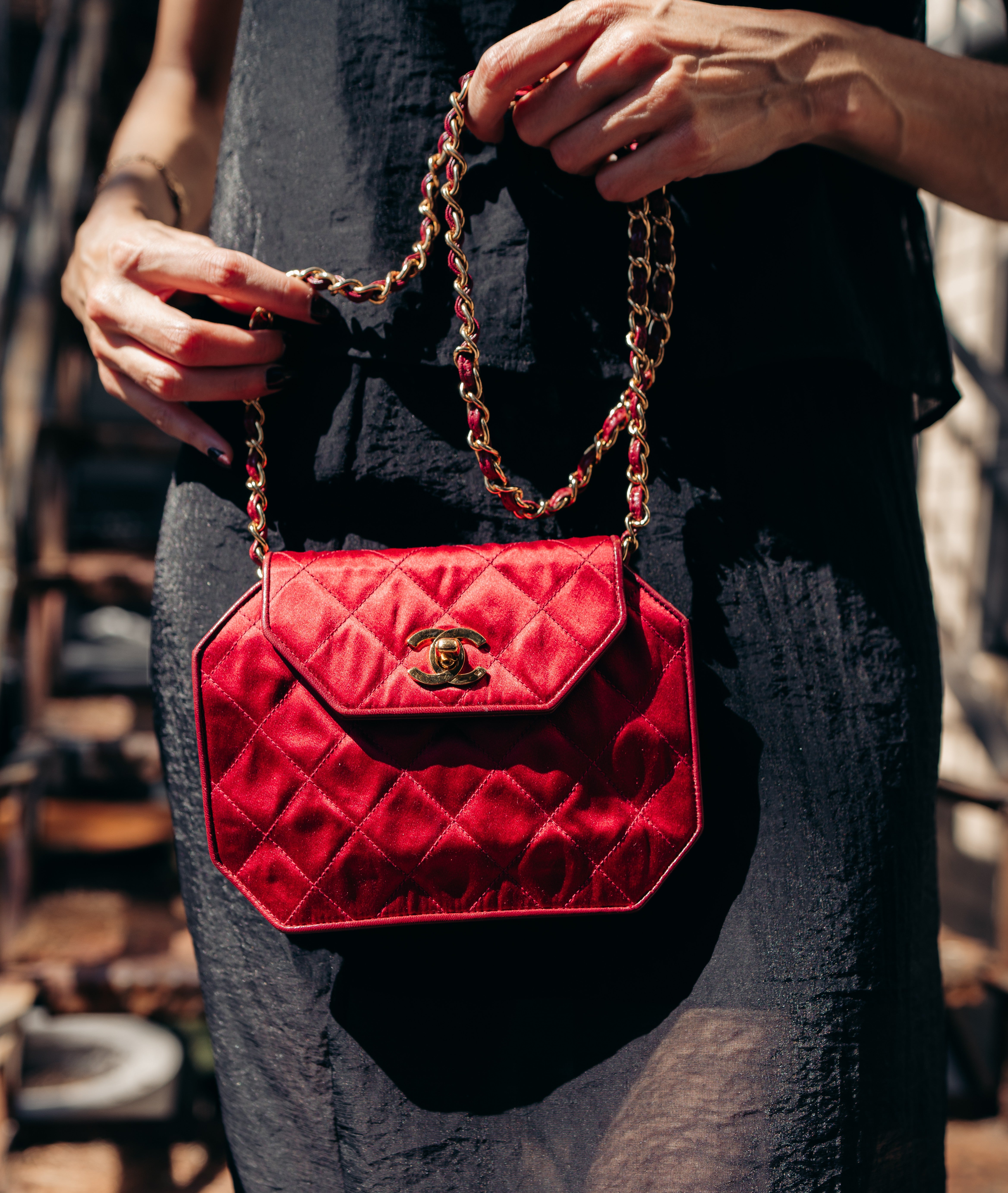 Chanel red octagon bag in satin with gold chain strap held by a person wearing a dark outfit.