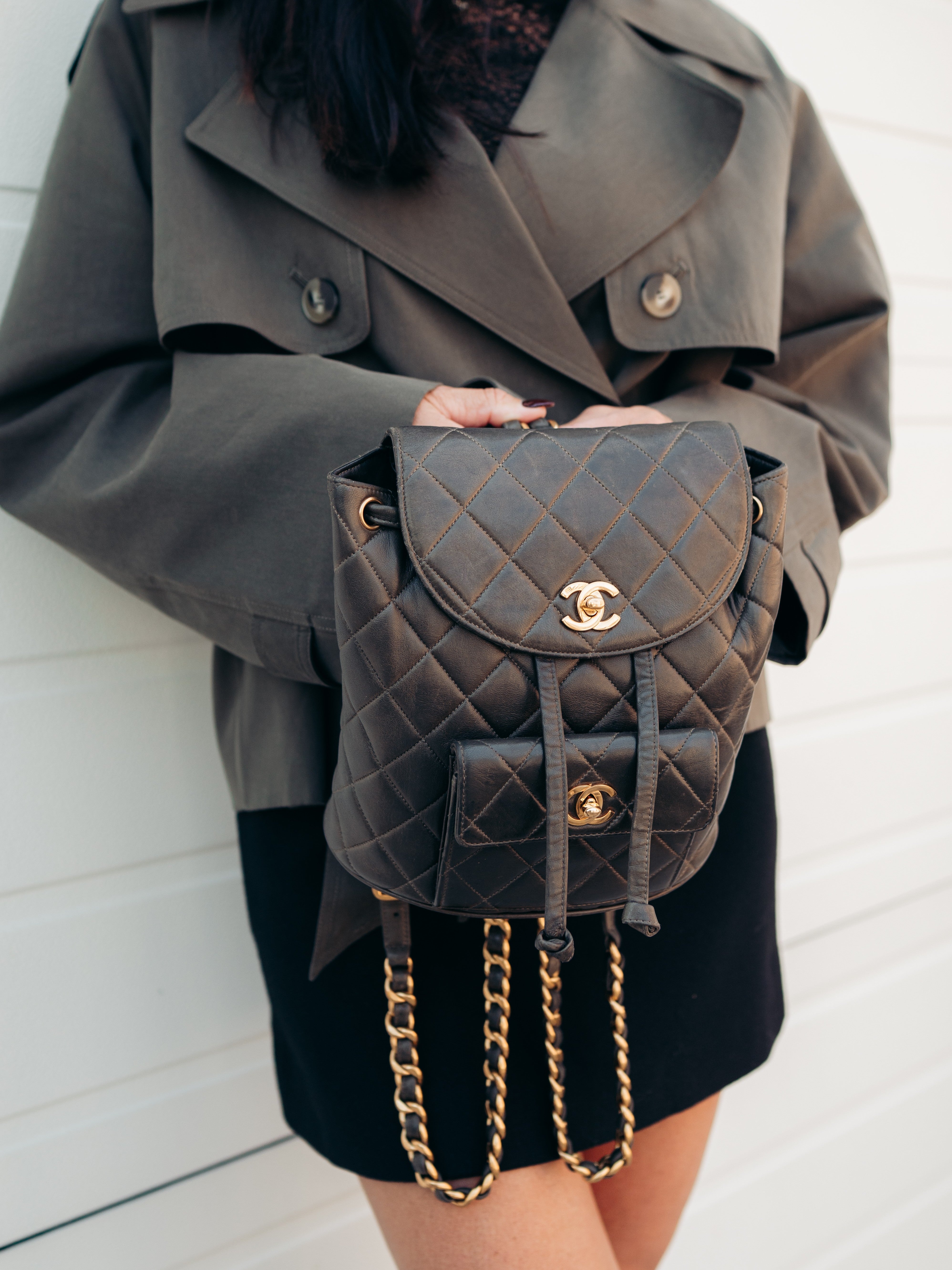 Person holding a Chanel duma backpack in olive green with a gold chain detail against a white background
