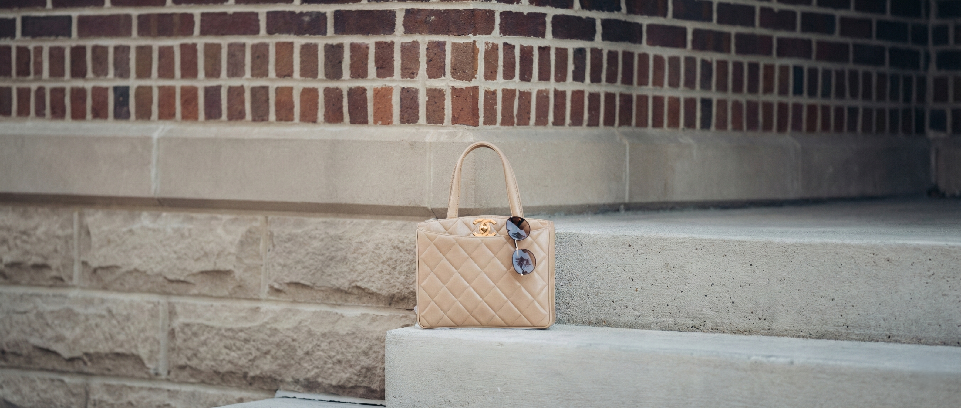 Chanel beige turnlock handbag on a stone step with a brick wall background
