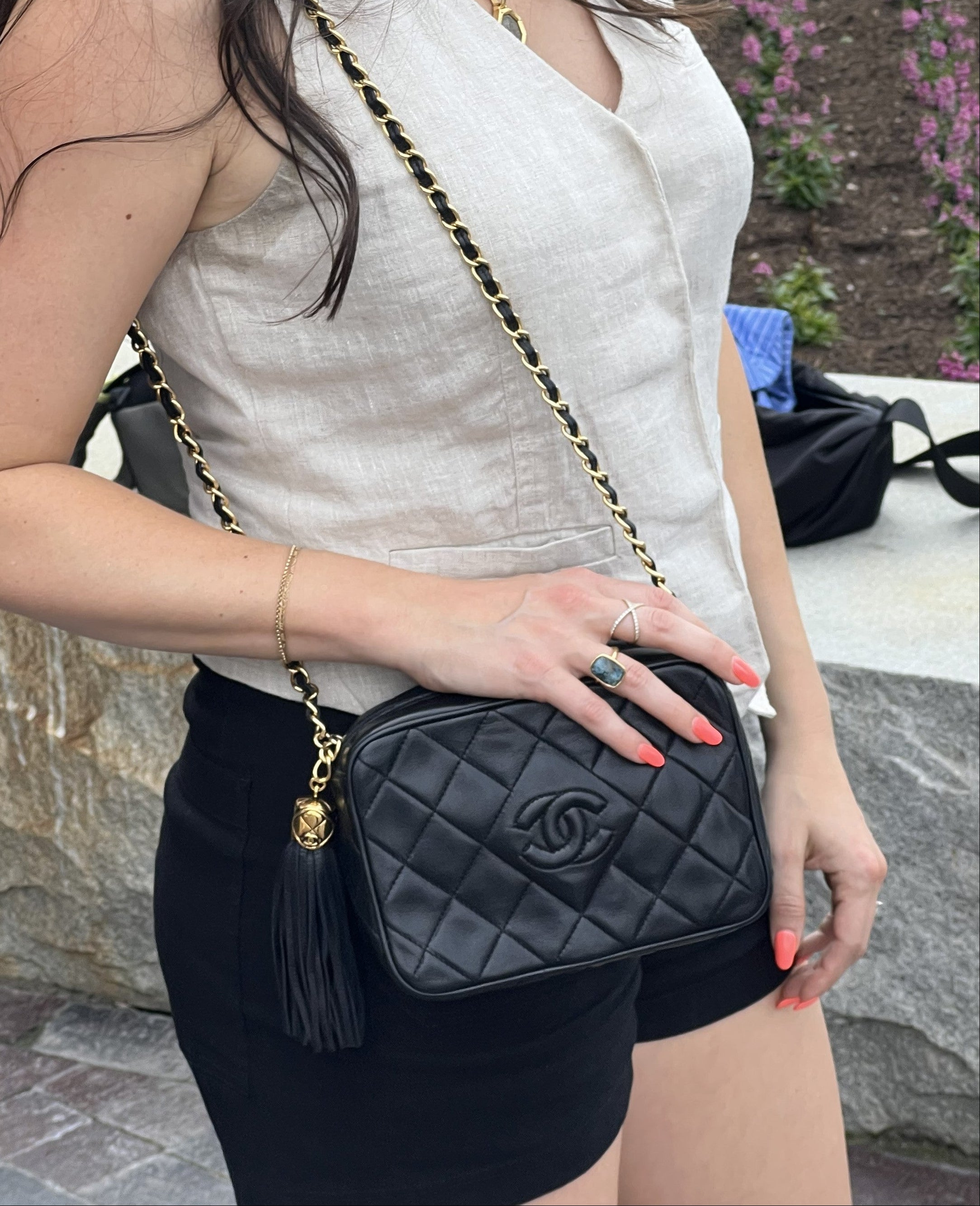 Person holding a Chanel black camera bag with a gold chain strap outdoors