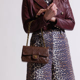 Person wearing a burgundy leather jacket and leopard print pants holding a brown Chanel small classic flap bag